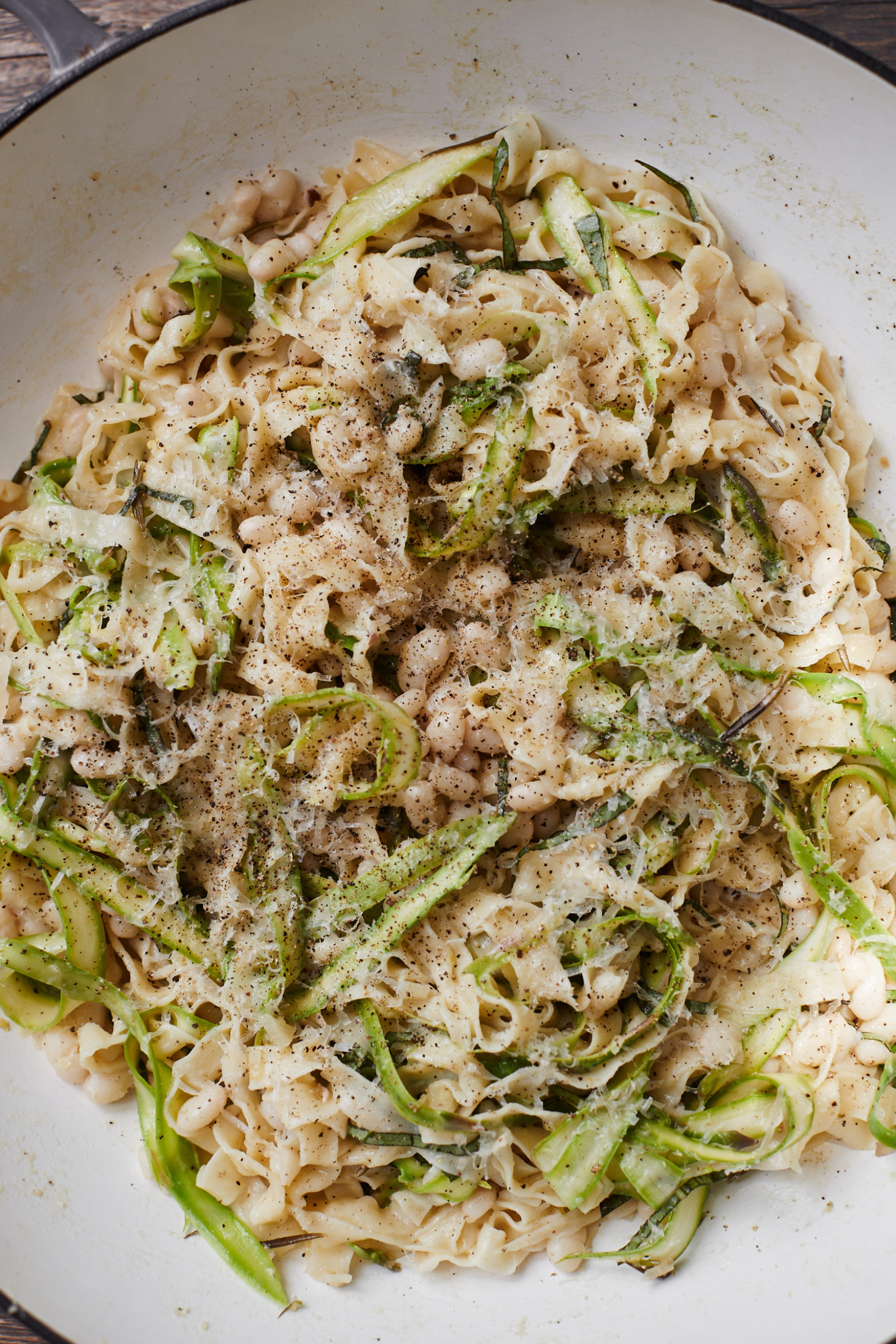 Close-up photo of pasta in a braiser tossed with shaved asparagus, white beans, basil, and parmesan