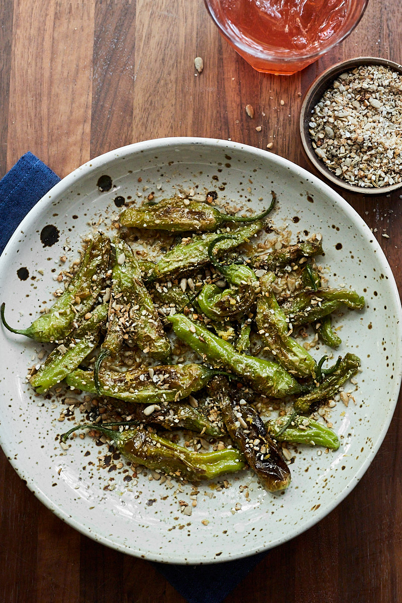 blistered shishito peppers dusted with a crushed buckwheat mixture in a speckled bowl