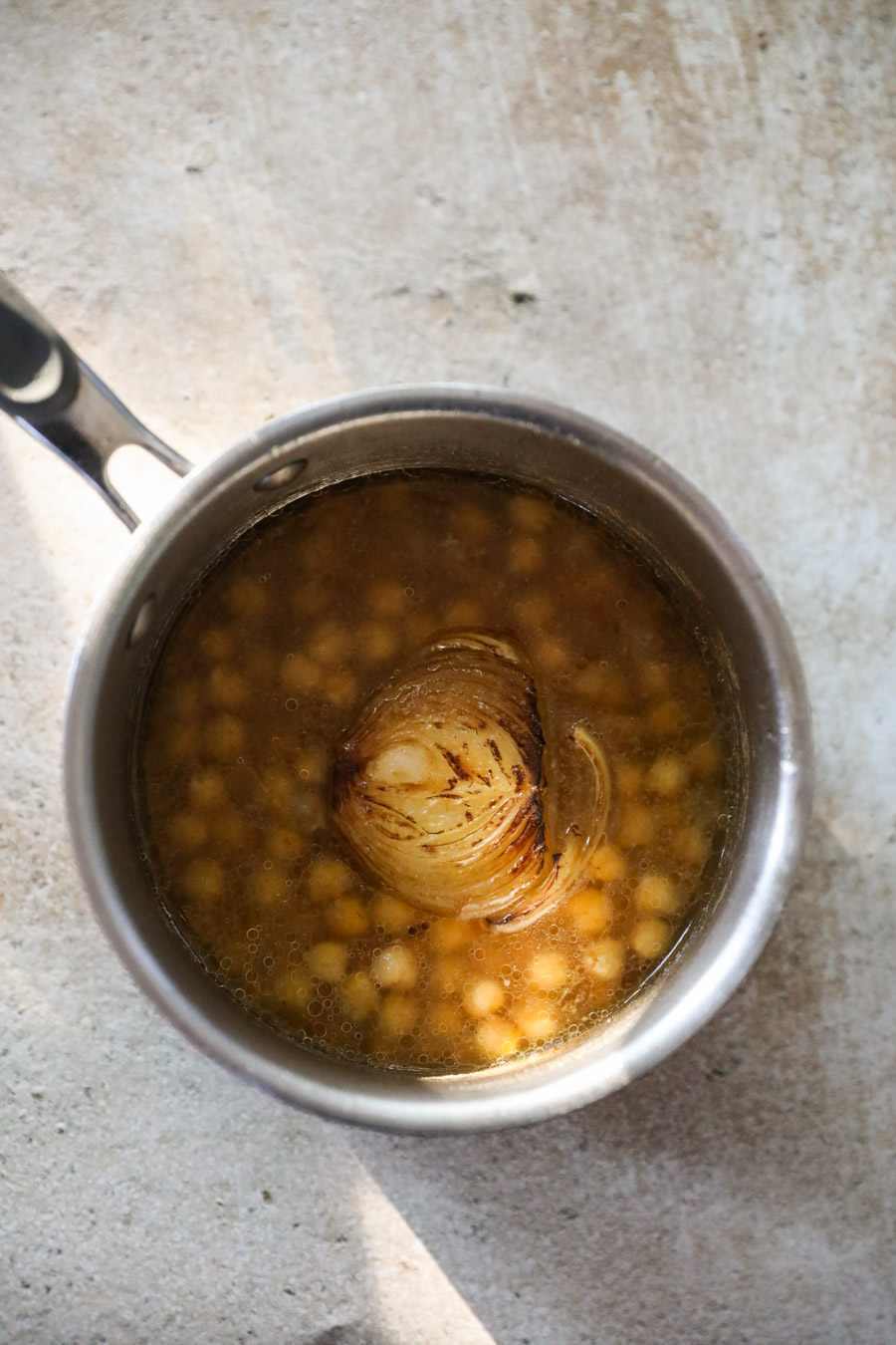 Small pot with chickpeas in broth and a charred onion half