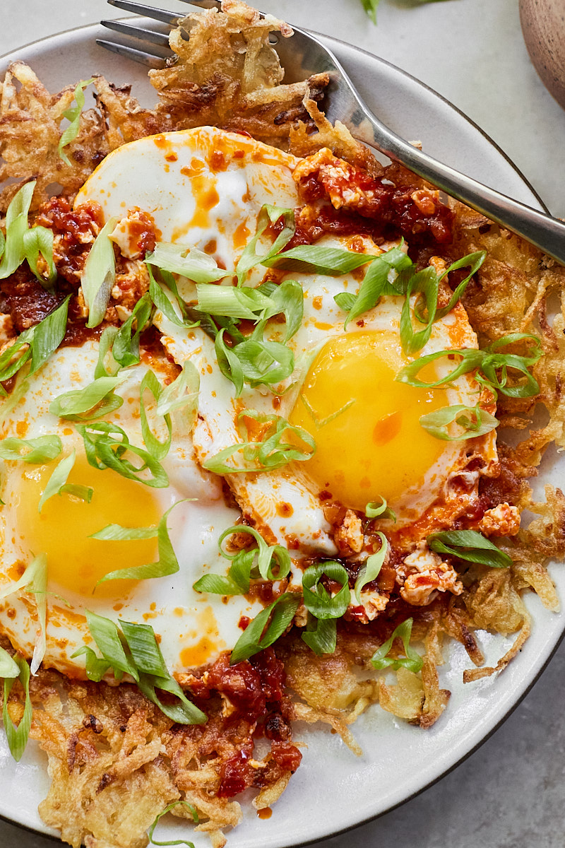 Close-up photo of crispy hash browns covering a plate, topped with a chile fried egg. 