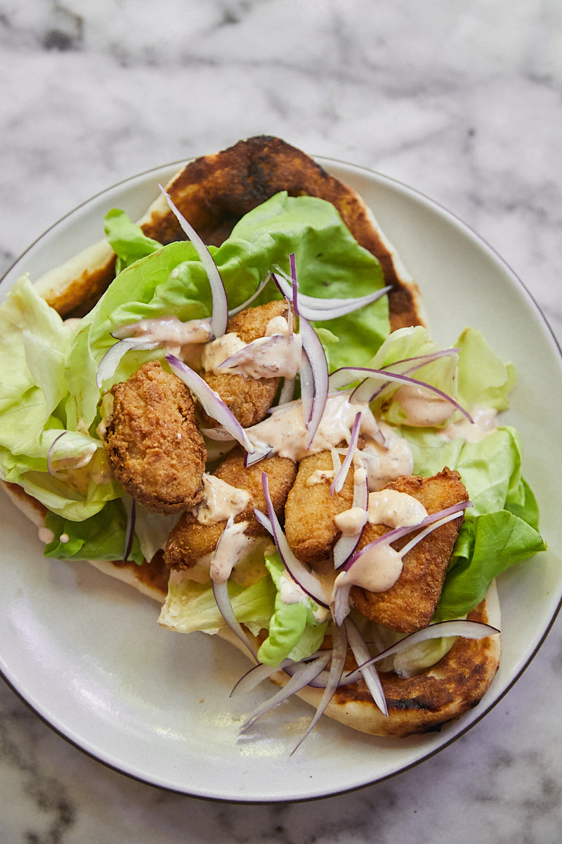 A photo of fried green tomato in a wrap with lettuce, slices of onions and a chipotle sauce drizzle on top. 