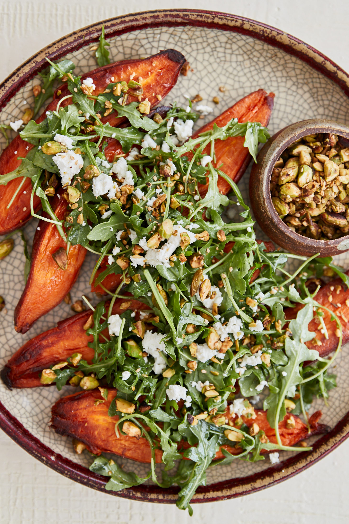 a light crackled plate with sweet potatoes topped with arugula and pistachios