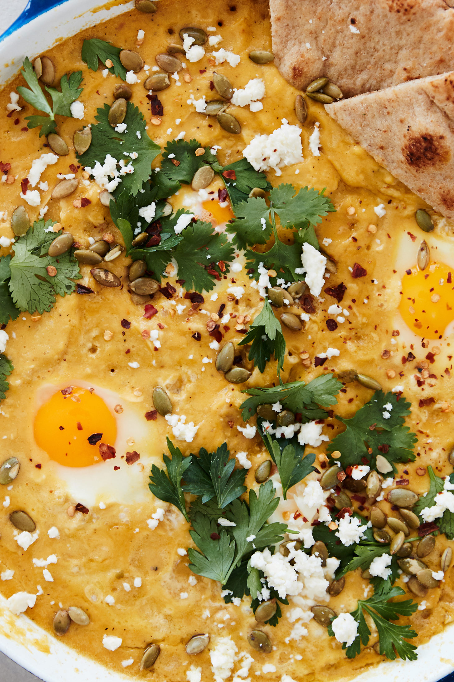 Close-up image of a creamy pumpkin sauce with eggs and topped with parsley and feta.