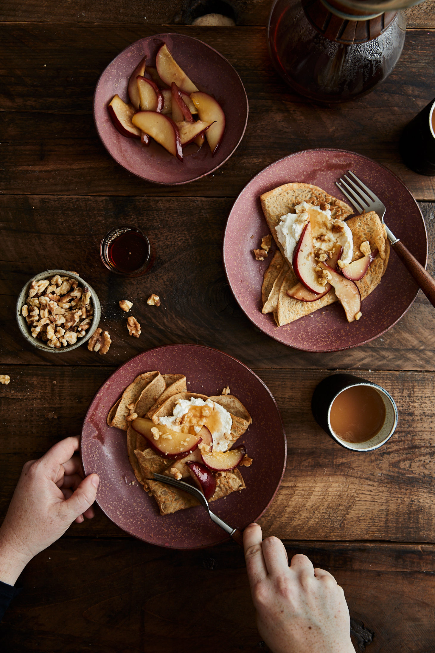 Image of two plates of crepes with pears and hands cutting into one of the crepes.