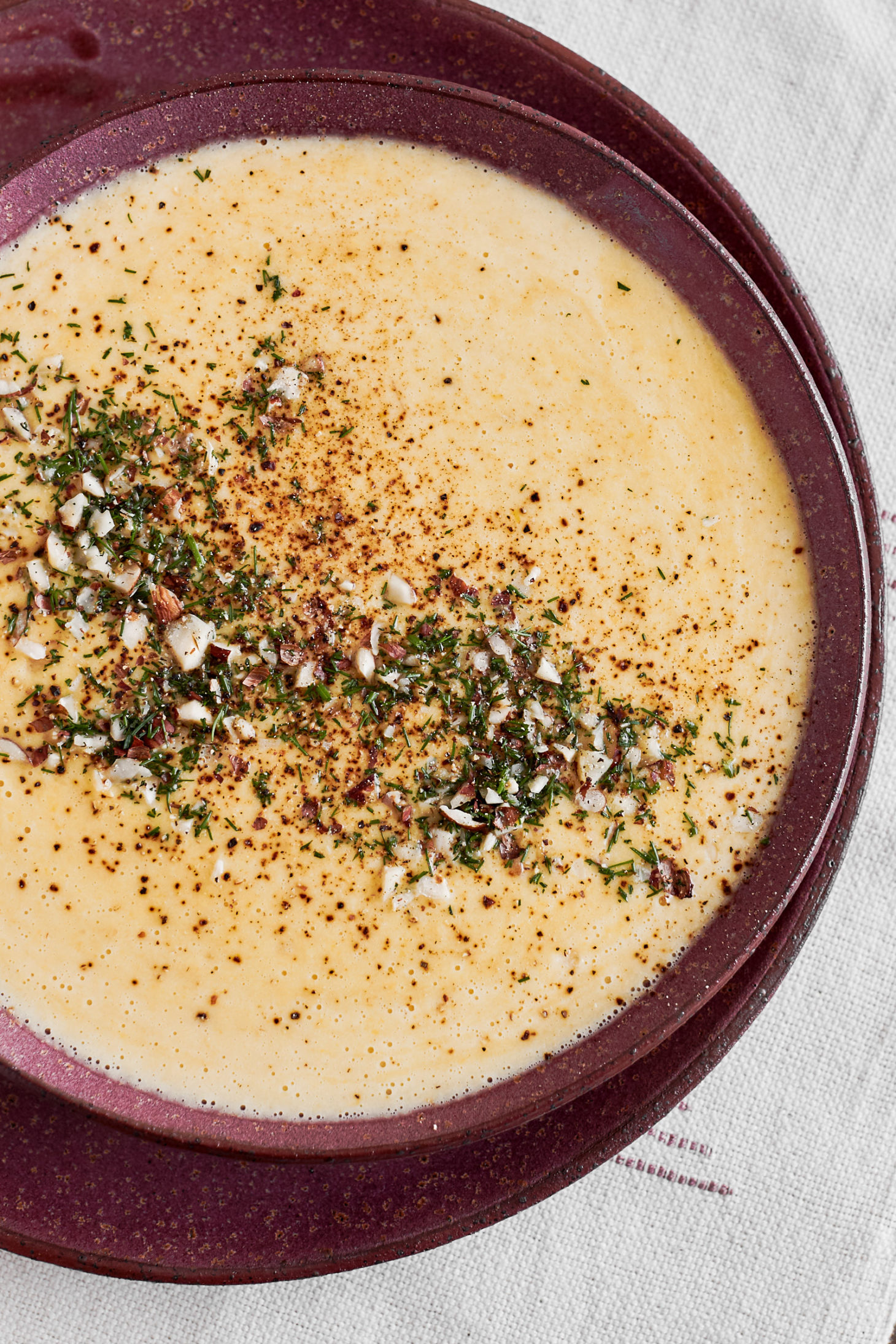 Close-up photograph of sweet corn soup with a dill garnish in a dark pink bowl.